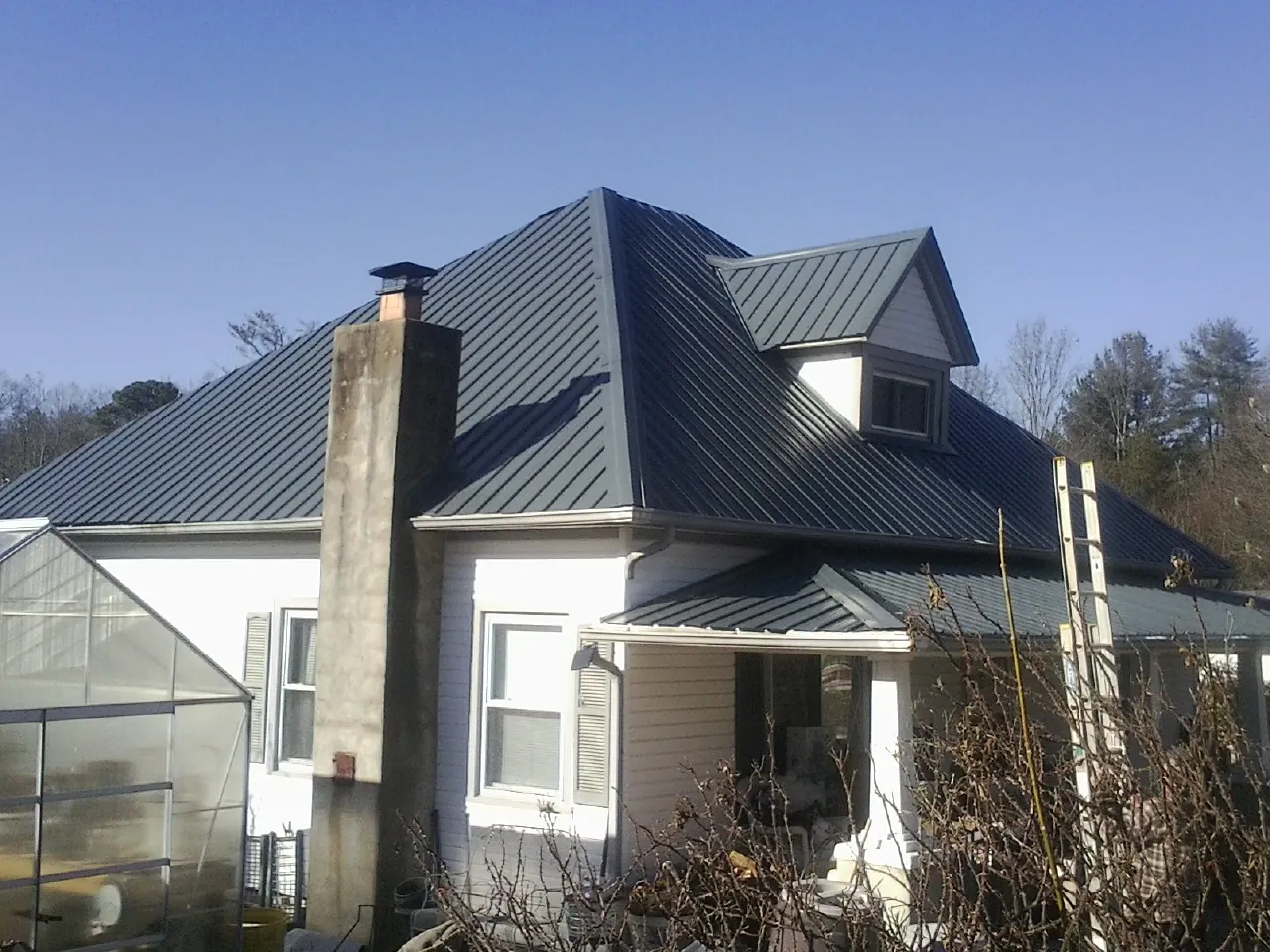 Dark blue standing seam metal roof on a white farmhouse with dormer — Slate & Tile Roof Repair by Roofing Brothers in Mojave
