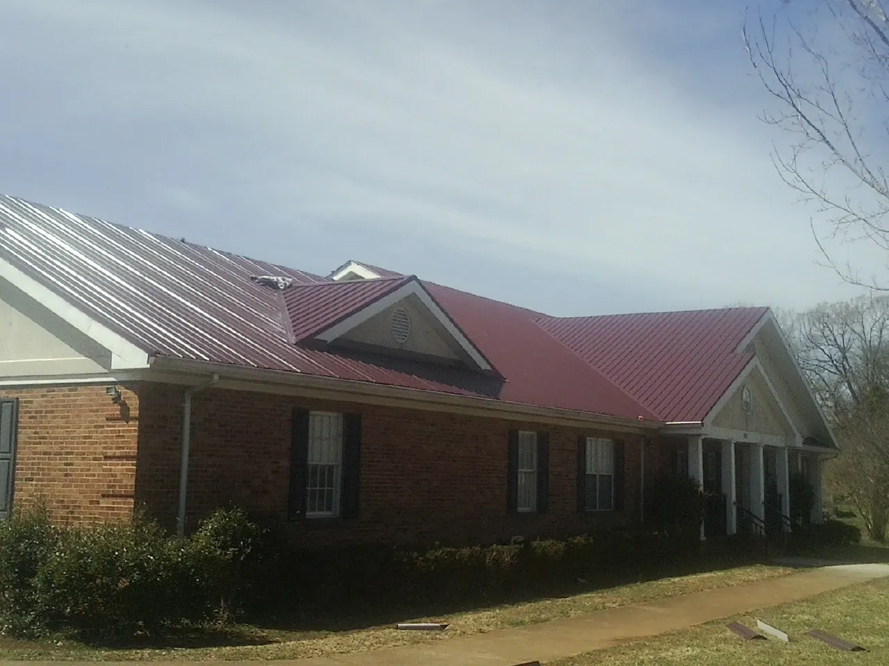 Red metal roof with gabled entries on a long brick building, from a Hail Damage Roof Repair job in Mojave
