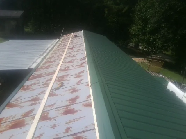 Old rusted panels beside newly installed green metal roofing — Wind Damage Roof Repair by Roofing Brothers in Mojave