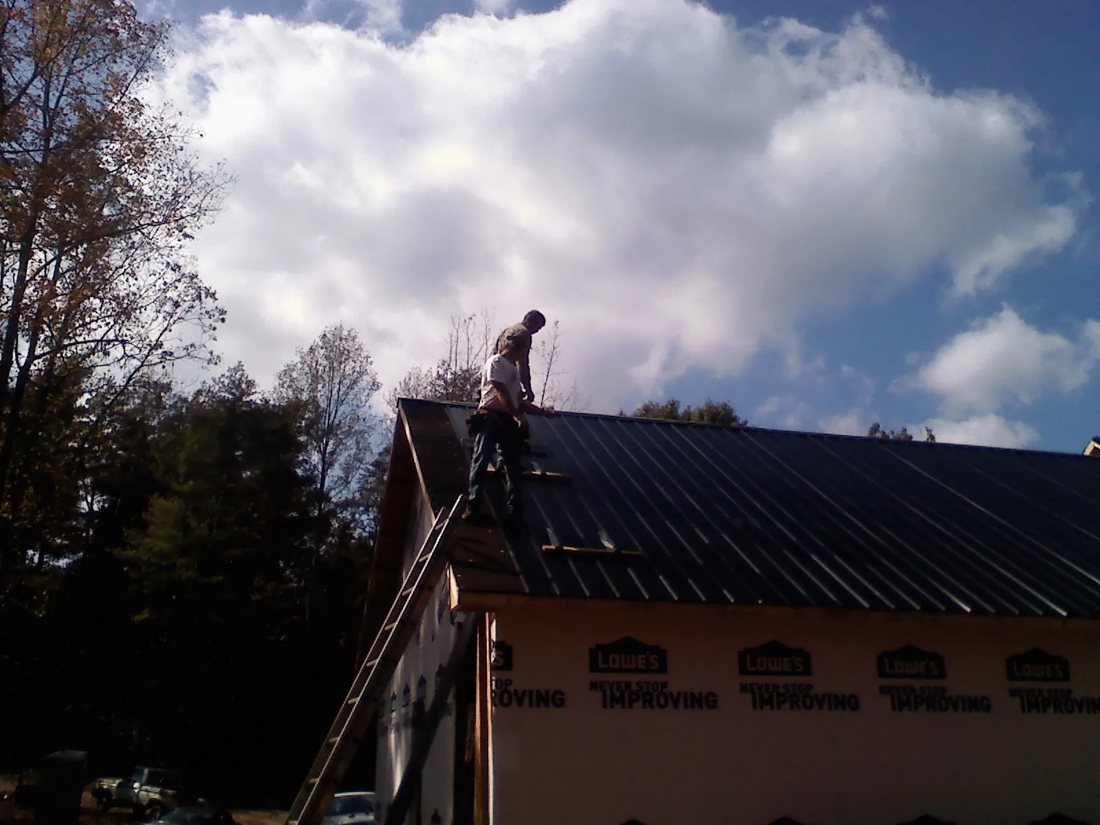 Roofer fastening dark metal panels high against a cloudy sky, from a Roof Inspection job in Mojave