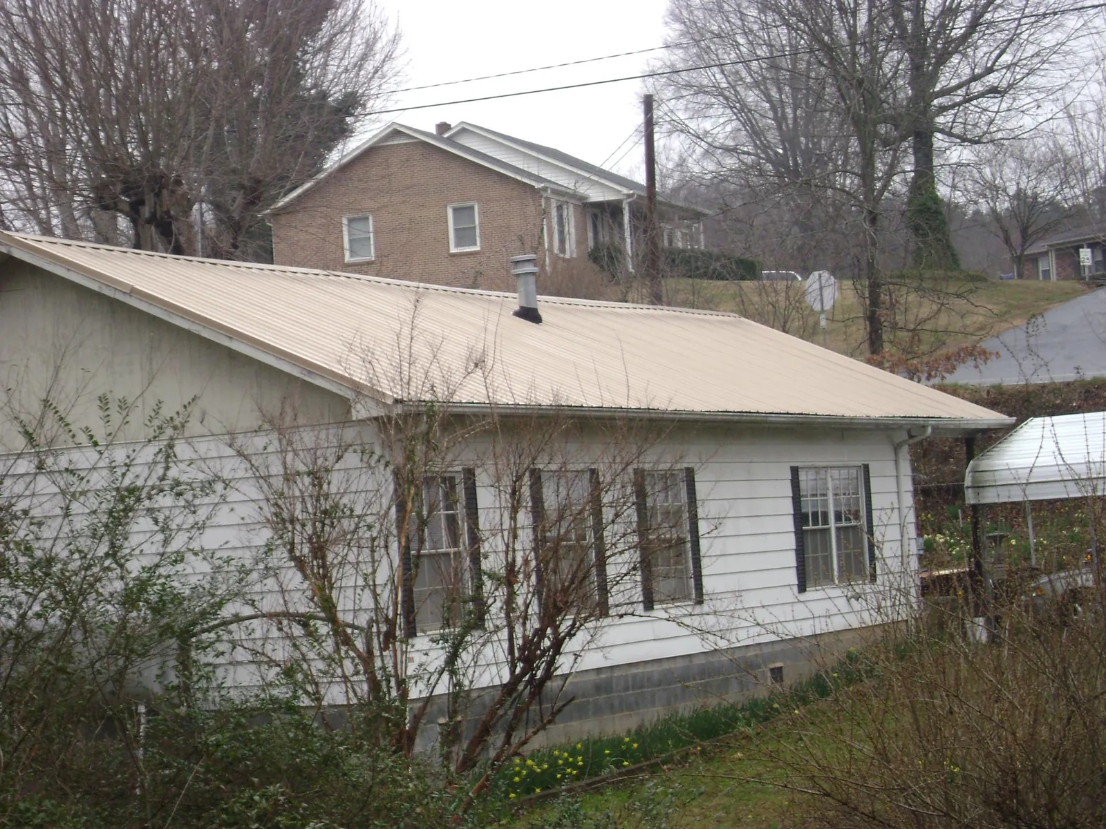 Tan metal roof on a white sided house set into a hillside — Commercial Roofing by Roofing Brothers in Mojave